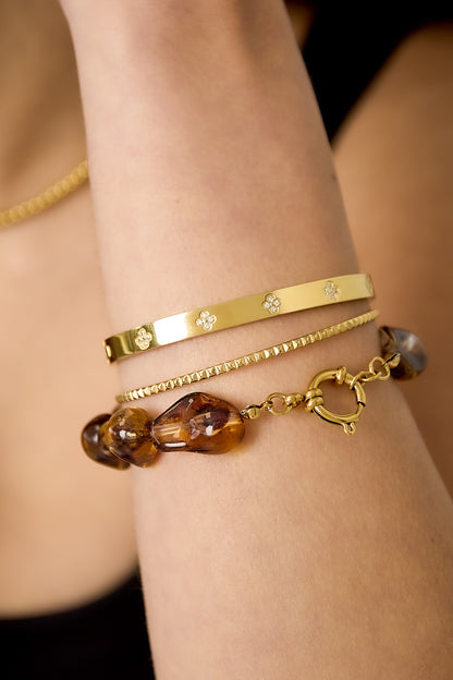 Close-up of a woman's wrist wearing an amber acrylic beaded bracelet stacked with gold bracelets