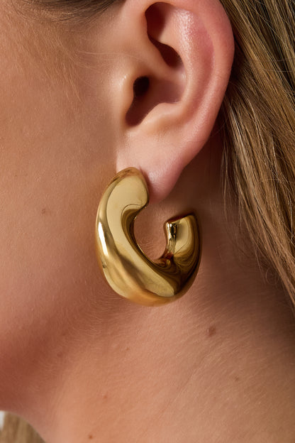 Close-up view of a woman wearing one chunky sculpted hoop earring in shiny gold showing fit and style