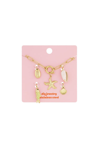 Gold stainless steel chain bracelet with dangling starfish, fish, and seashell charms on a pink display card.