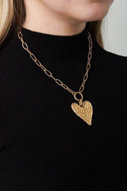 Woman wearing a gold-plated hammered heart pendant necklace paired with a black top