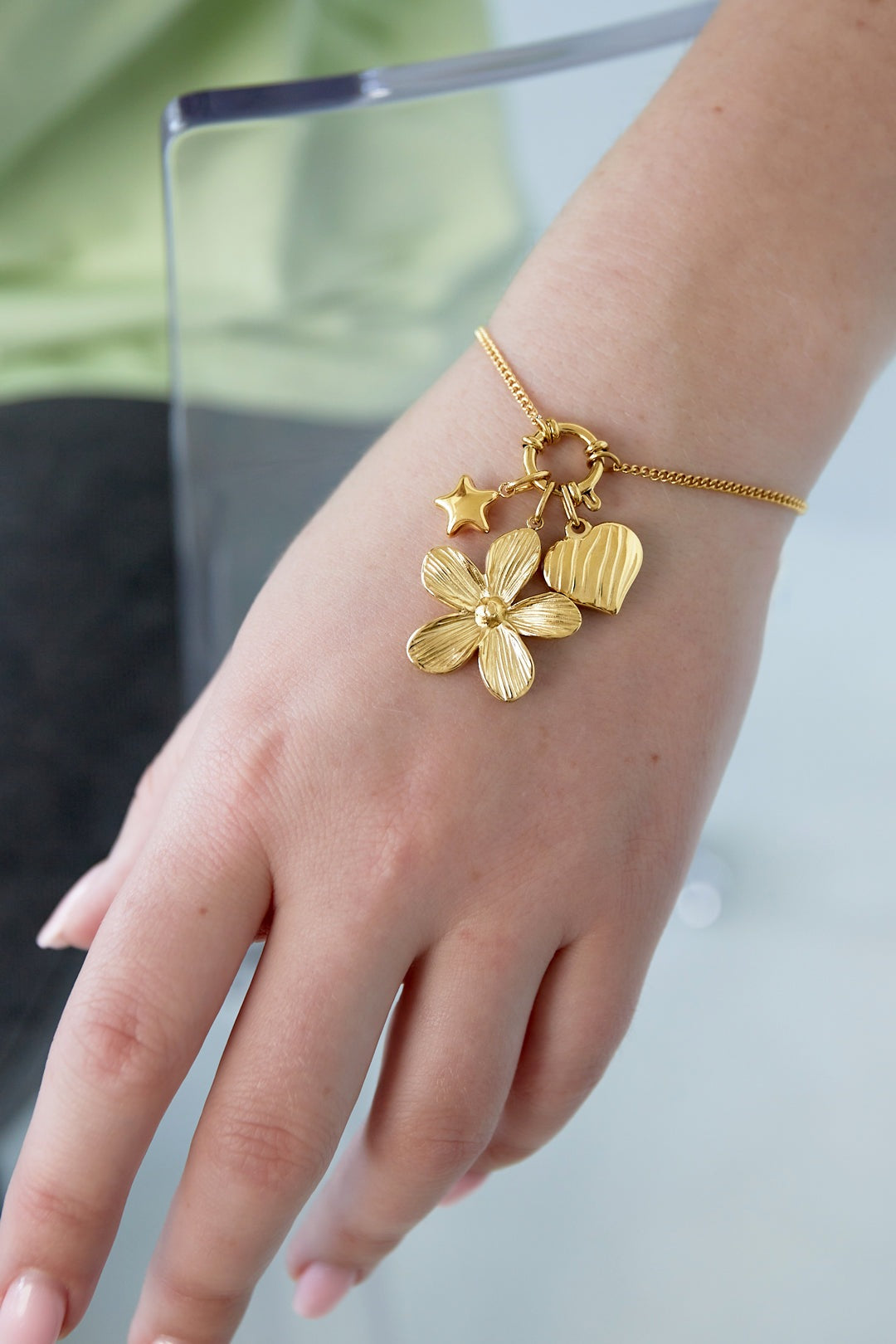 Close-up of gold charm bracelet worn on wrist showing flower, heart, and star charms in detail