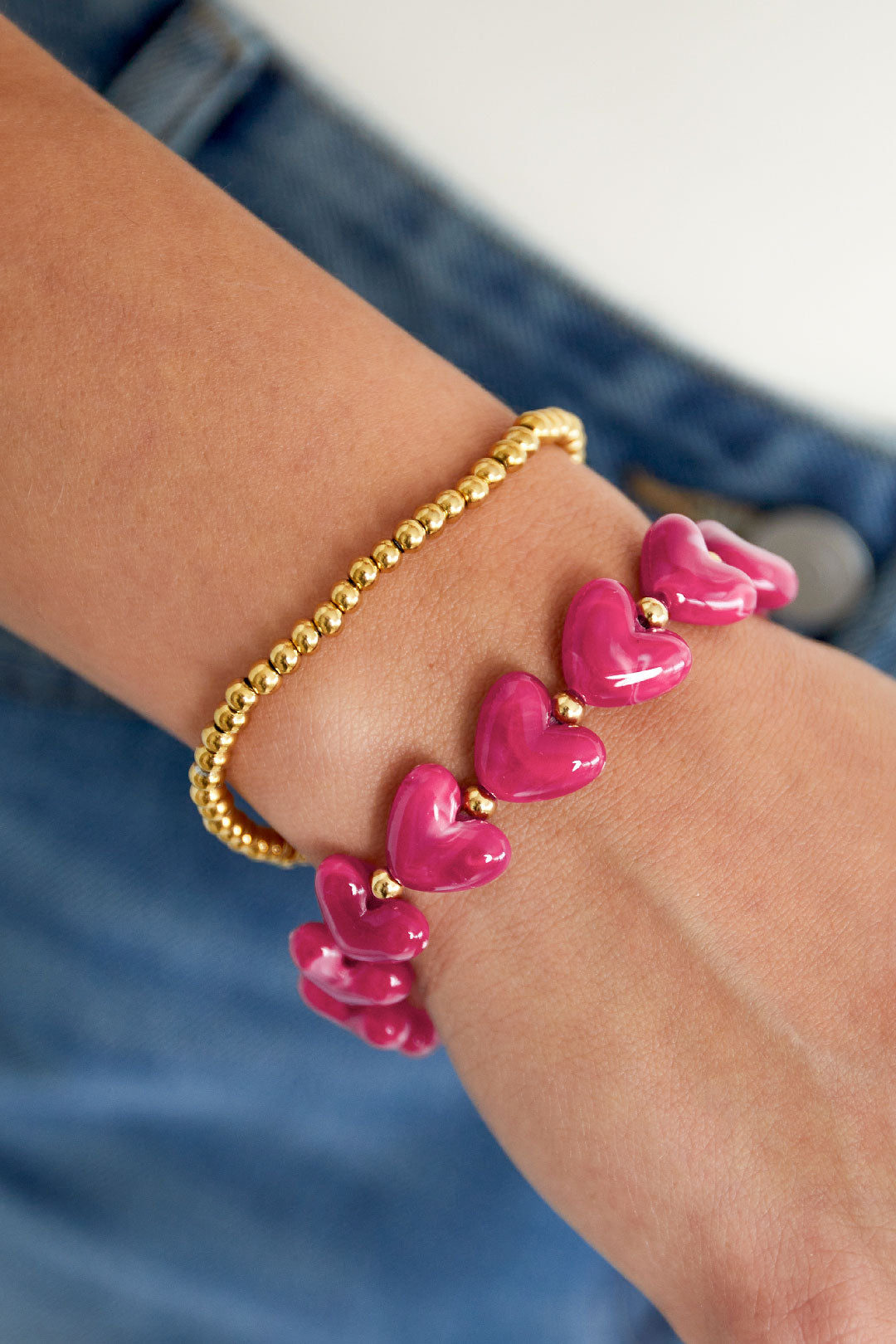 Close-up of pink heart beaded bracelet worn on wrist alongside gold bead bracelet