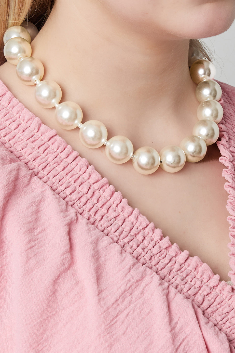 Model wearing the pearl statement necklace with large faux pearls, styled with a pink textured top showcasing the necklace's chic and youthful aesthetic