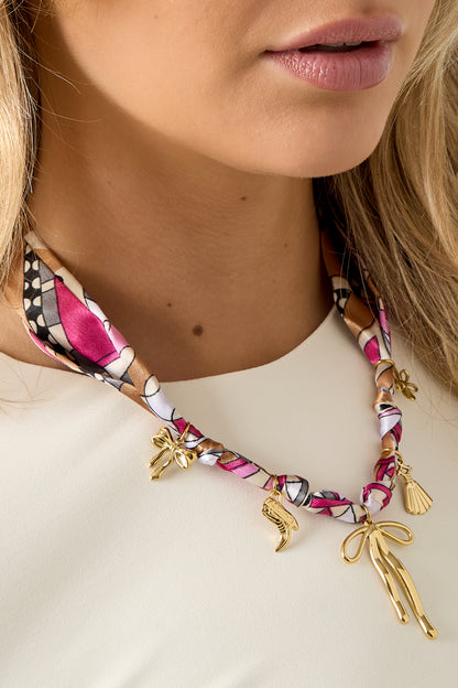 Close-up of the scarf necklace charms and texture wrapped around the woman's neck highlighting the vibrant colors and glossy gold accents.