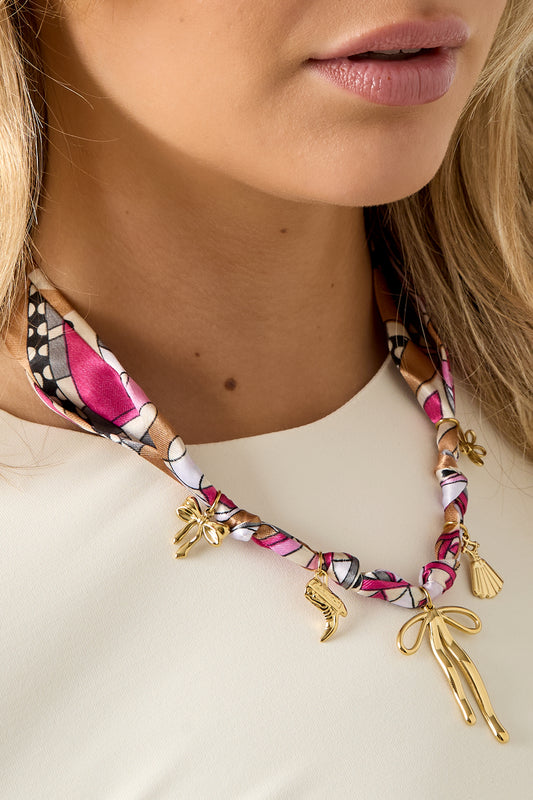 Close-up of the scarf necklace charms and texture wrapped around the woman's neck highlighting the vibrant colors and glossy gold accents.