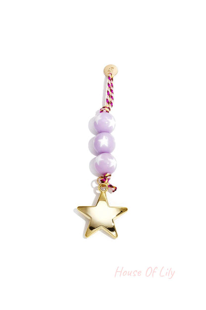Close-up of pastel purple bead charm with shiny gold star pendant and braided cord