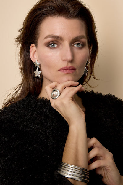 Close-up of a woman wearing silver star-shaped double drop earrings, black fuzzy sweater, and silver rings and bracelets