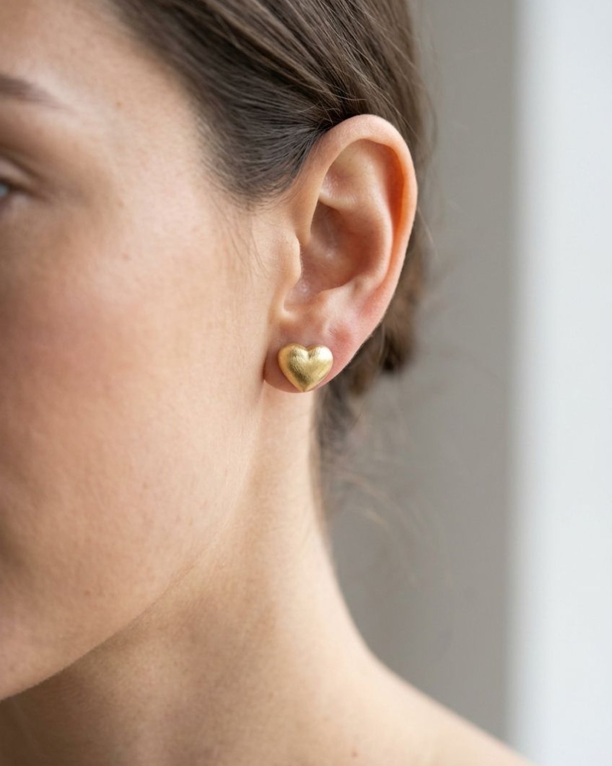 Small brushed stainless steel heart stud earring worn on a model's earlobe for a romantic and simple look.