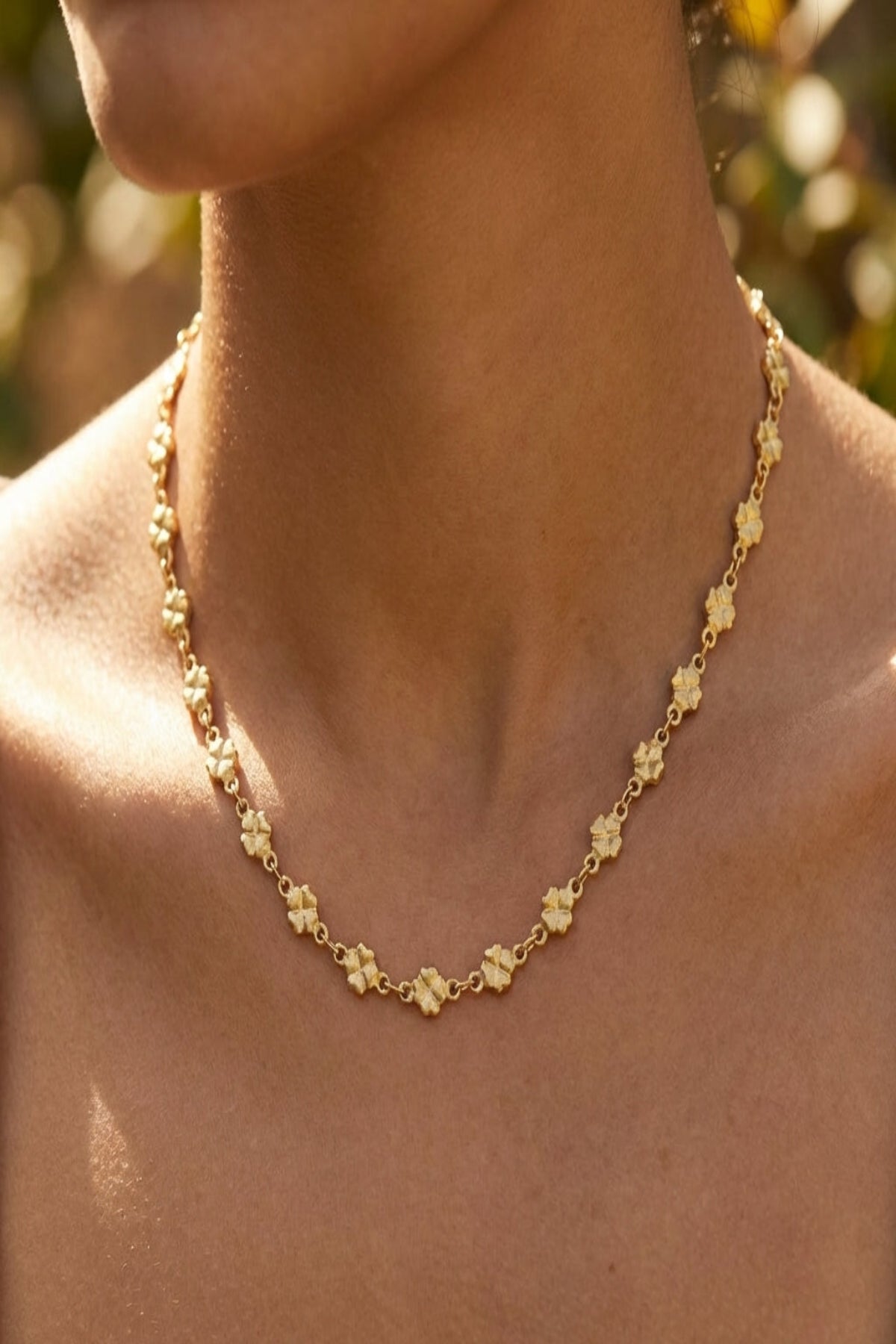 Close-up of delicate clover link necklace in natural light, highlighting fine micro-texture and youthful elegance on model.