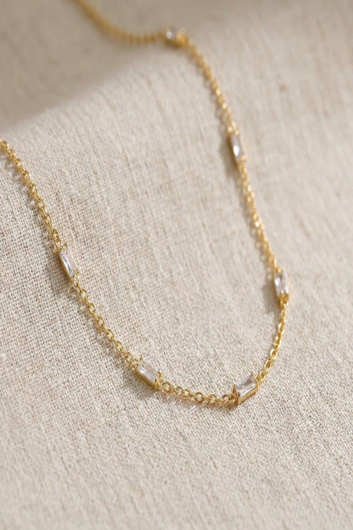 Close-up of a delicate crystal chain necklace with tiny zircon accents, showcasing fine craftsmanship and subtle shimmer on a neutral background.