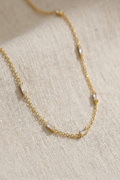 Close-up of a delicate crystal chain necklace with tiny zircon accents, showcasing fine craftsmanship and subtle shimmer on a neutral background.
