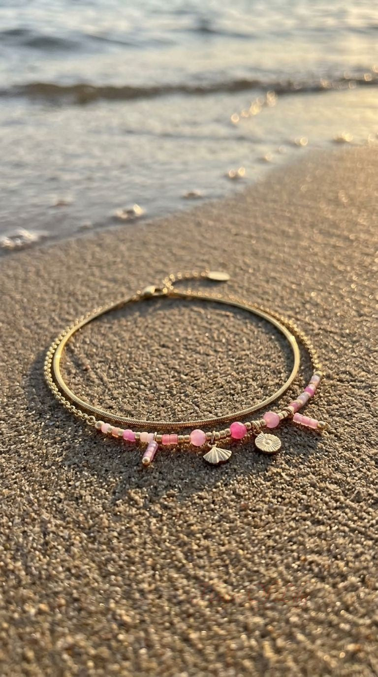 Double layer anklet with pastel beads, shell and sun charms resting on sand during golden hour, highlighting its delicate design.
