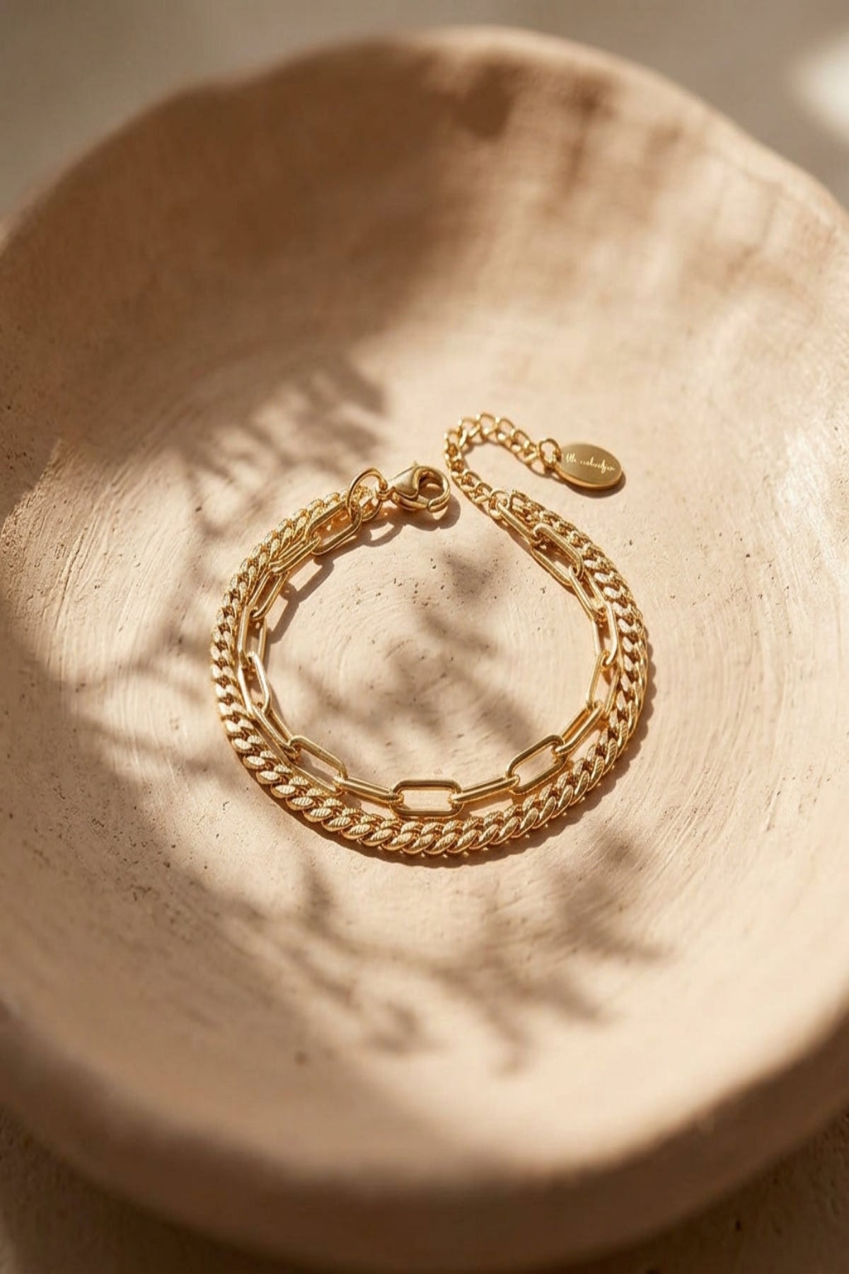 Close-up of a small, double-layered stainless steel bracelet on a textured clay background, highlighting its irregular shape and reflective surface.