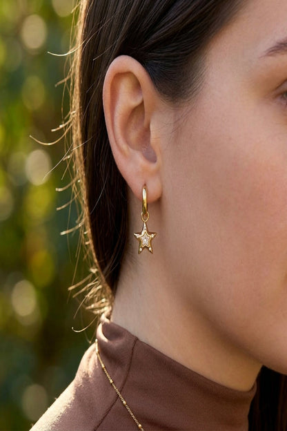Close-up of 'earrings superstar' drop earrings with rhinestones and stainless steel, shown on a model's ear against a blurred outdoor background.