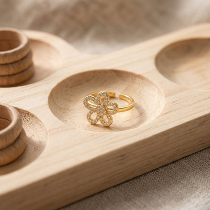 Close-up of a petite floral statement ring made of stainless steel with rhinestones, focusing on its petal design and sparkle on a wooden display tray.