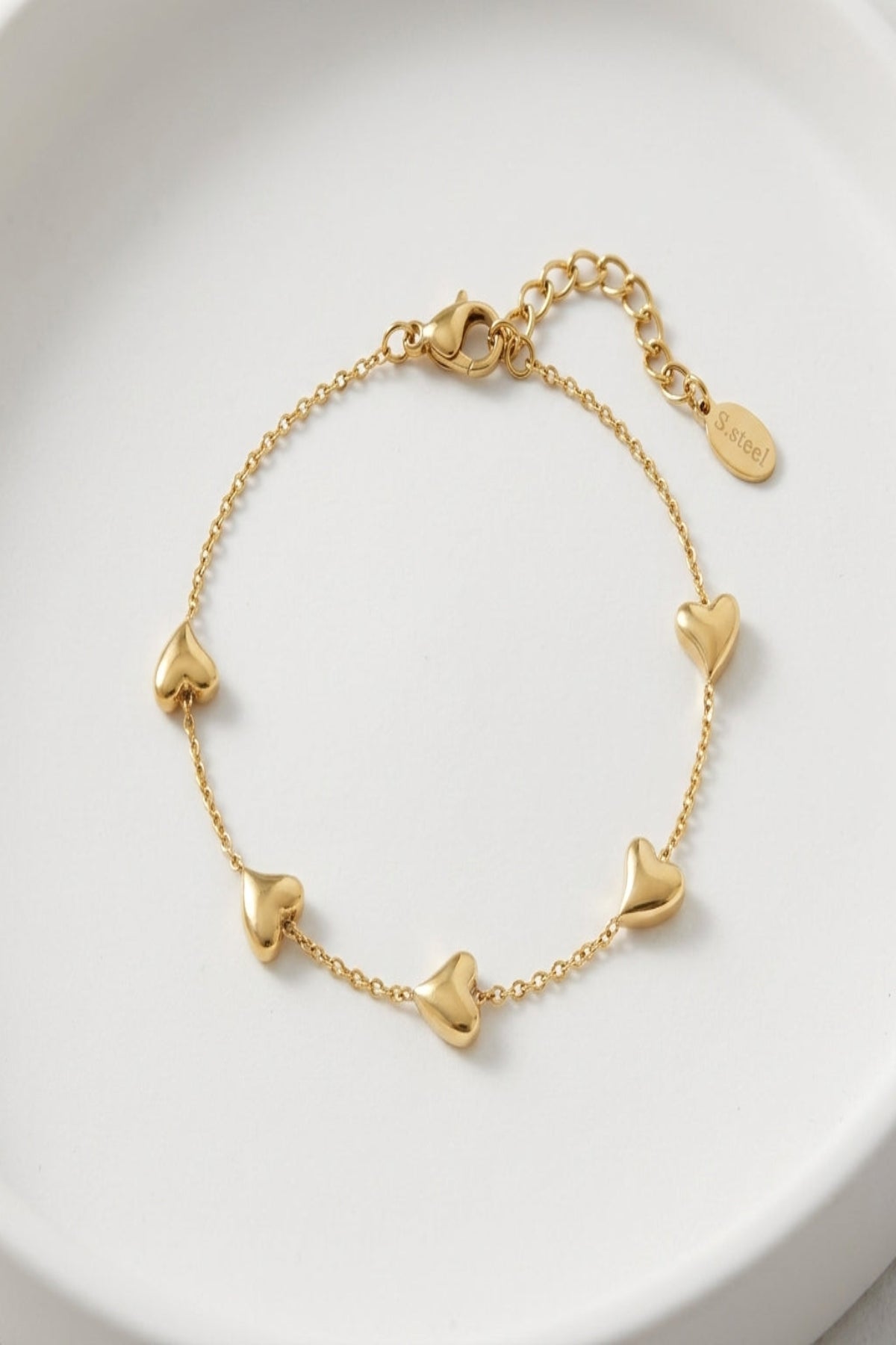 Close-up of a tiny gold charm bracelet with lobster clasp on a smooth white background, showcasing fine links and micro-texture.