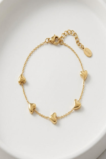 Close-up of a tiny gold charm bracelet with lobster clasp on a smooth white background, showcasing fine links and micro-texture.