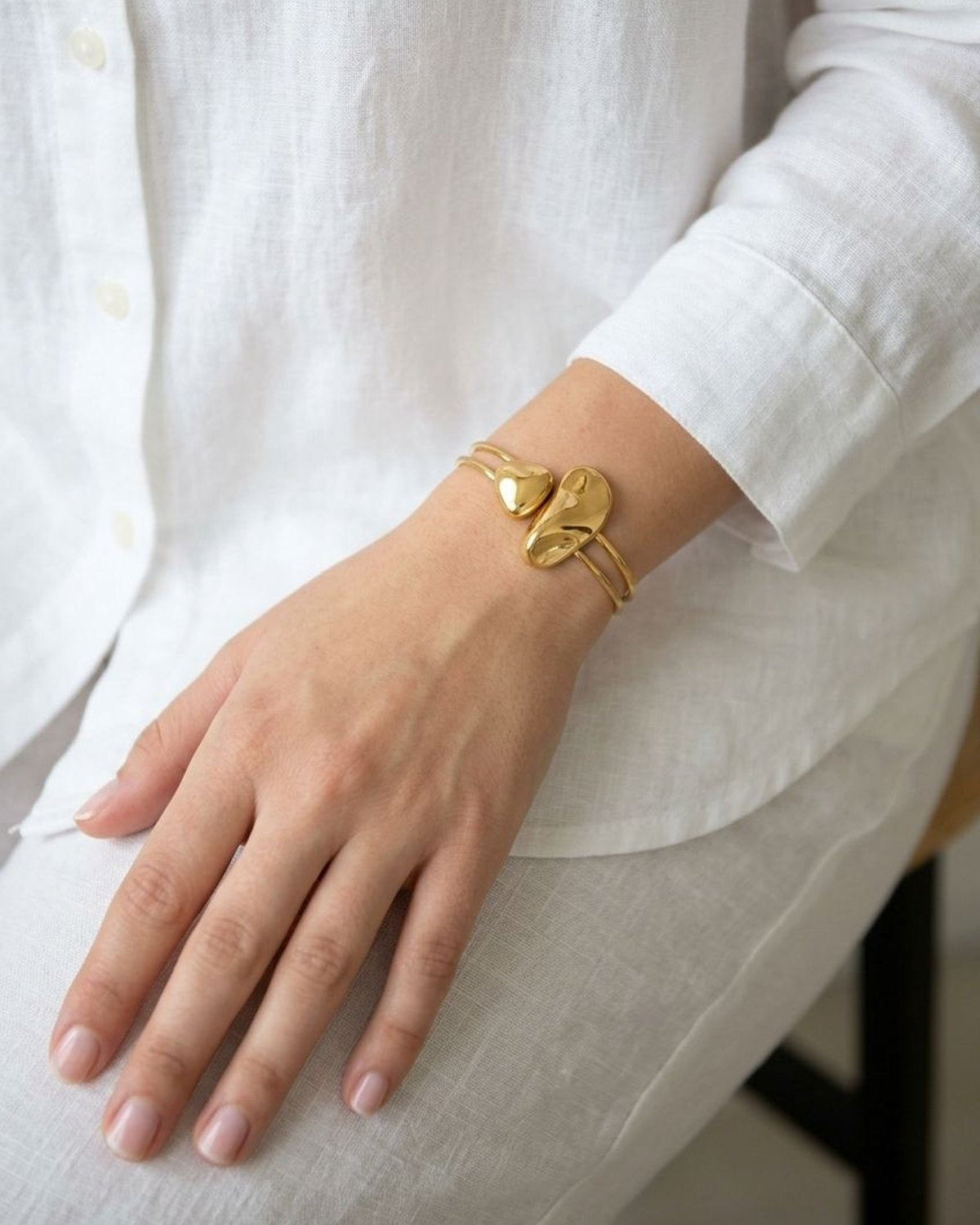Small gold cuff with smooth organic contours worn on a wrist with a simple white linen shirt.