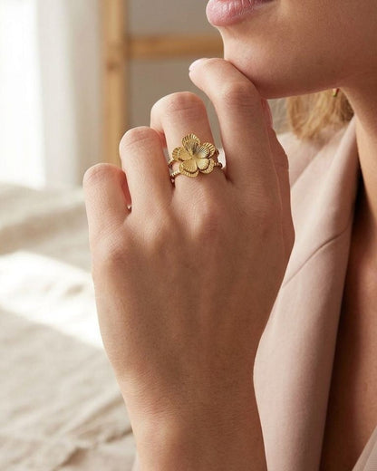 Small gold-toned alloy flower ring with sculpted petals and fine grooves displayed on a wooden surface with natural soft lighting.
