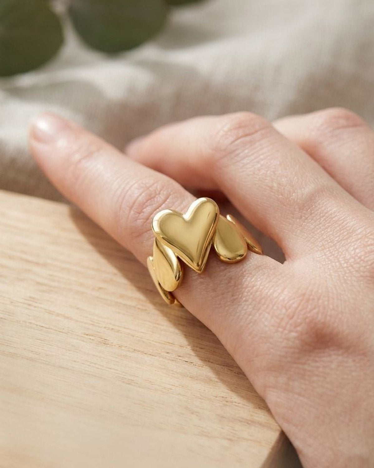 Small gold heart statement ring on natural textured wooden surface with warm daylight highlighting its smooth contours and metallic shine.