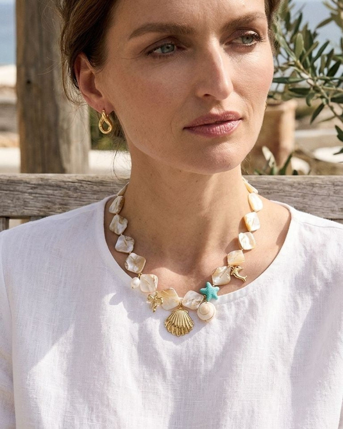 Small gold mother-of-pearl shell earrings with iridescent shimmer on rustic wood, highlighting their elegance and shell shape.