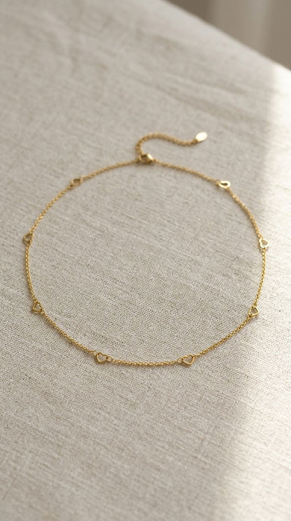 Small gold-plated stainless steel heart chain necklace draped on soft fabric, highlighting its fine texture and feminine style.