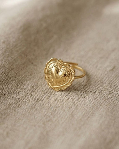 Small gold-tone hammered heart ring with scalloped edges on beige fabric, highlighting textured finish and vintage-inspired design.