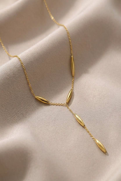 Close-up of a small, elegant gold Y-shaped necklace resting on neutral silk fabric, highlighting its fine chain and polished beads with soft natural lighting.