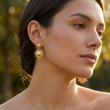 Small 'Golden Sun Heart Dangles' earrings on a model in a sunny outdoor setting, catching light and highlighting their delicate design.