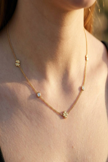 High-resolution close-up of a petite gold Lucky Clover Chain Necklace worn on a female model's collarbone, featuring tiny clover charms and sparkling rhinestones in warm golden hour lighting.