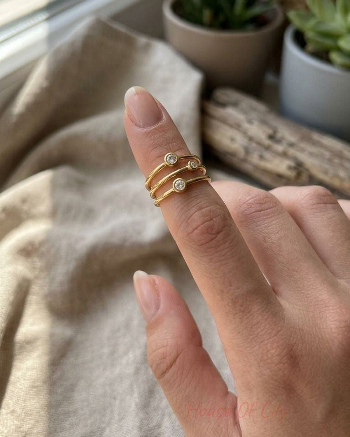 Small, delicate multi-band ring with bezel-set stones on a model's finger tip, in natural light highlighting its sparkle and fine texture.