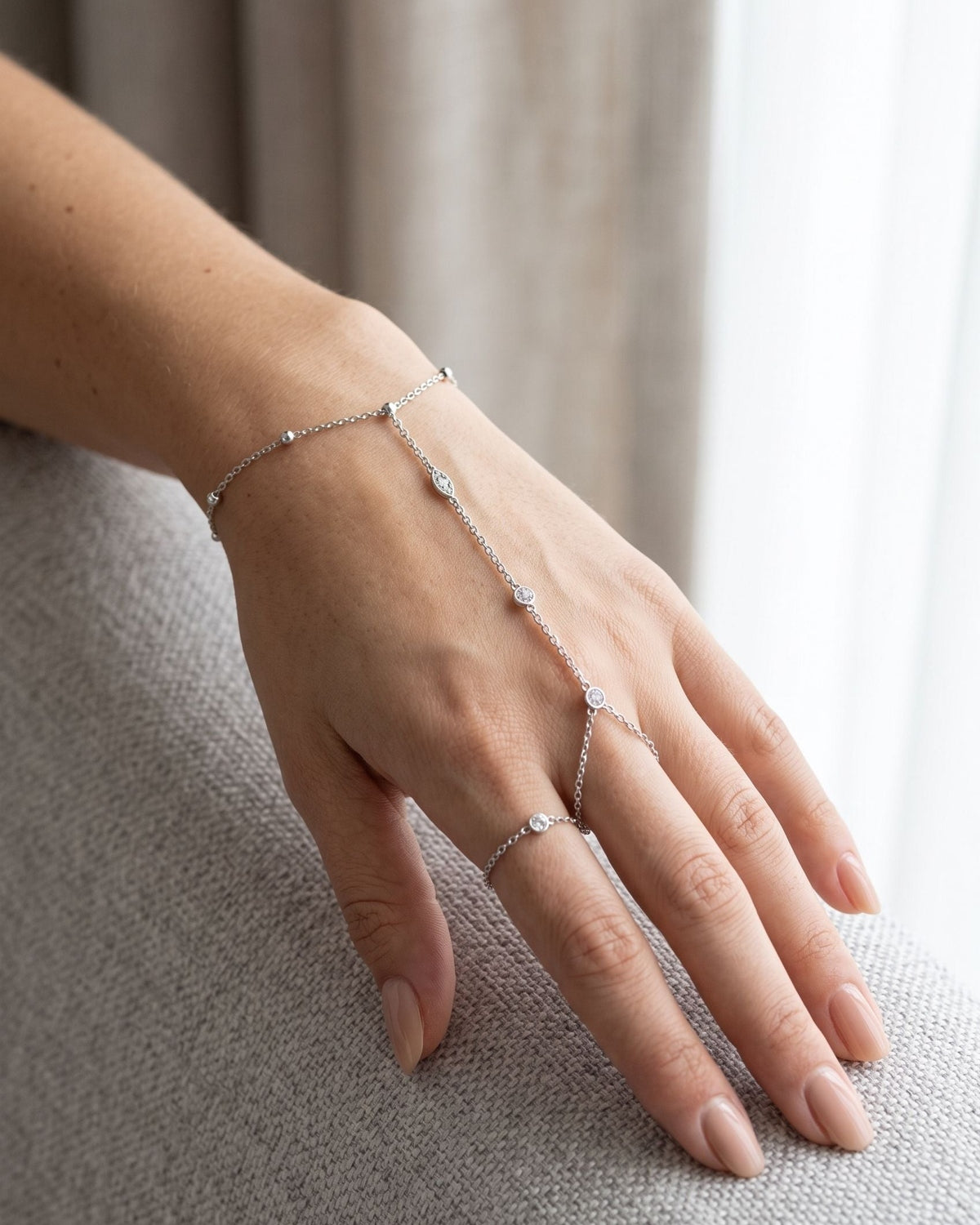 Woman wearing a delicate, minimalist rhinestone hand chain as a subtle accessory on her hand.