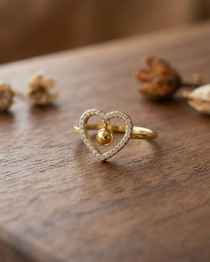 Small sculptural heart motif ring with high-shine finish on wooden surface, natural lighting emphasizing sleek stainless steel and elegant design.