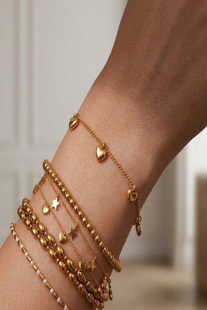 Close-up of a stainless steel bracelet with gold-tone heart charms on a neutral background.