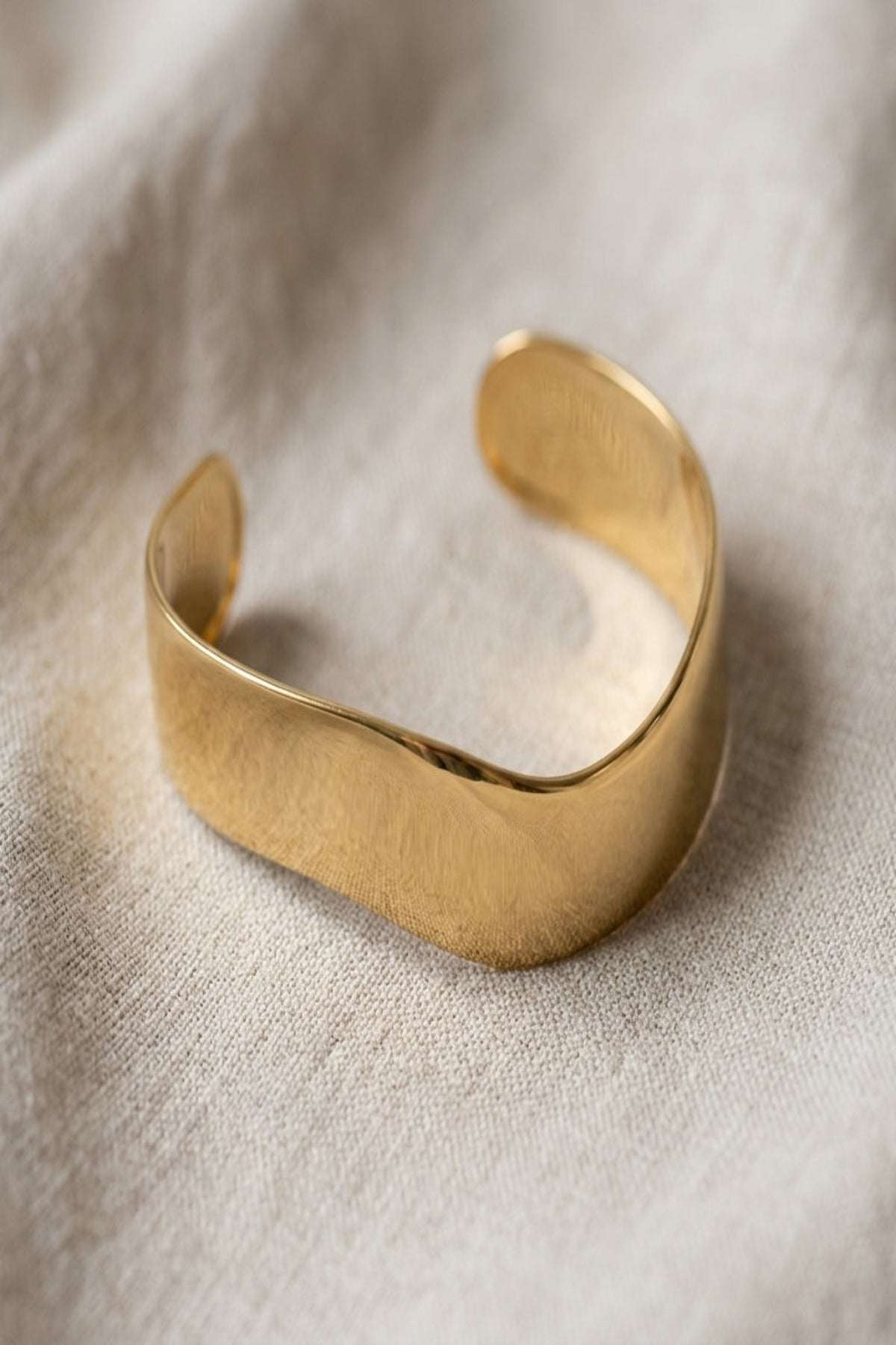 Close-up of a tiny stainless steel cuff bracelet with irregular shape and open ring connector on neutral fabric.