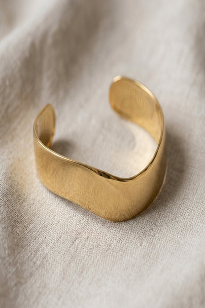 Close-up of a tiny stainless steel cuff bracelet with irregular shape and open ring connector on neutral fabric.