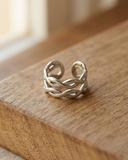 Miniature stainless steel ring with a double twist design on a wood surface, lit by natural light, highlighting its sculptural interwoven silhouette.