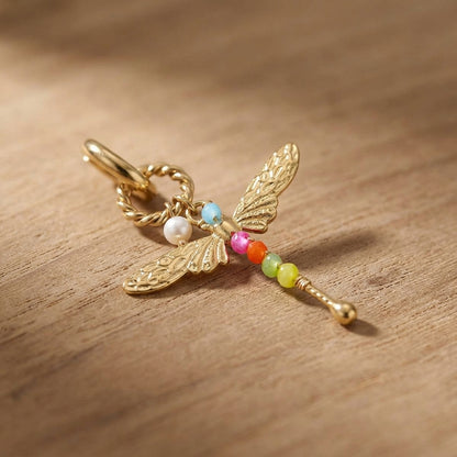 Small stainless steel dragonfly earrings with butterfly back, resting on textured wood surface, showcasing fine details and shape.