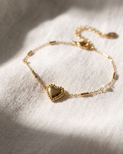 Dainty stainless steel heart charm bracelet with zircon resting on textured white linen fabric.