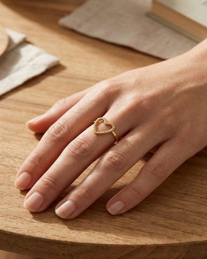 Small stainless steel heart ring, 2cm high, resting on a wood surface, highlighting its minimalist design and polished finish.