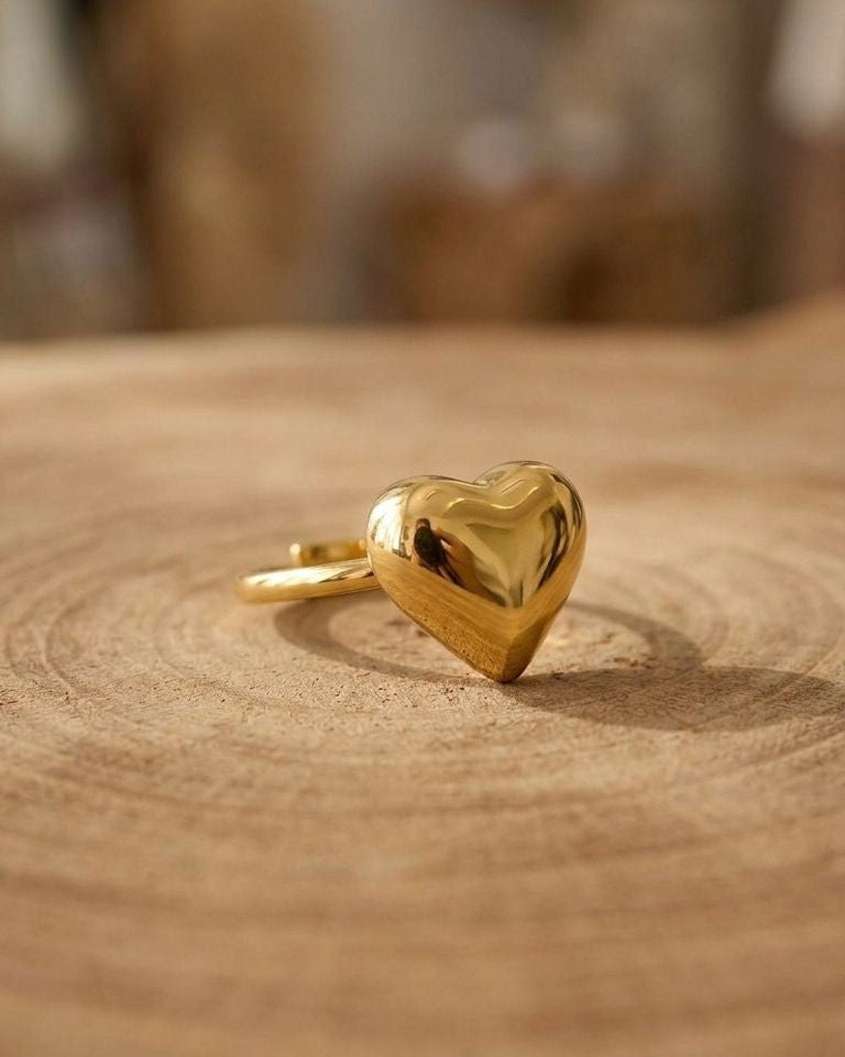 Close-up of a stainless steel Puffy Gold Heart ring with mirror finish, resting on a wooden surface, showcasing its plush heart silhouette and shine.
