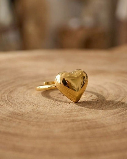 Close-up of a stainless steel Puffy Gold Heart ring with mirror finish, resting on a wooden surface, showcasing its plush heart silhouette and shine.