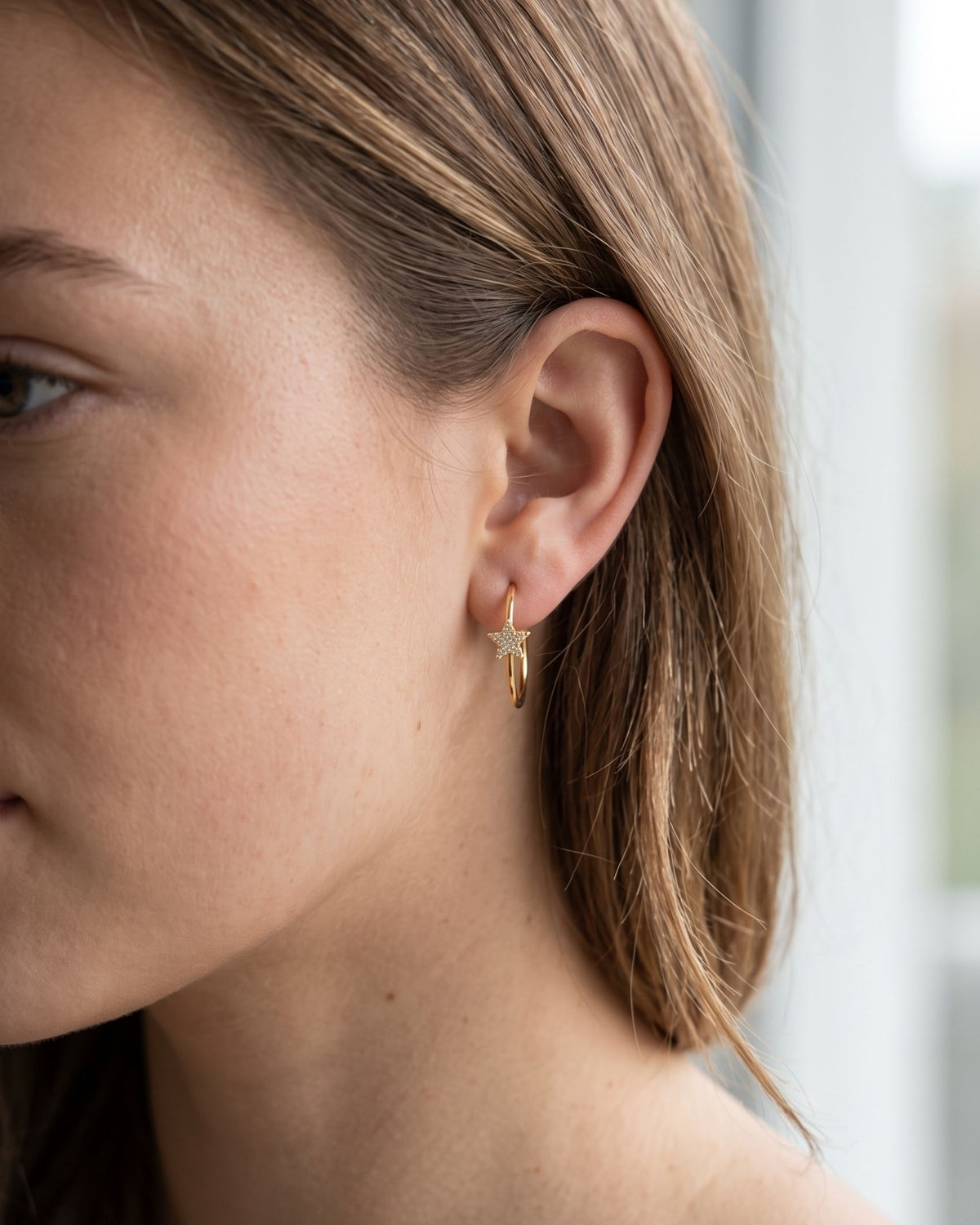 A close-up of a woman wearing a tiny stainless steel hoop earring featuring a delicate star-shaped rhinestone design.