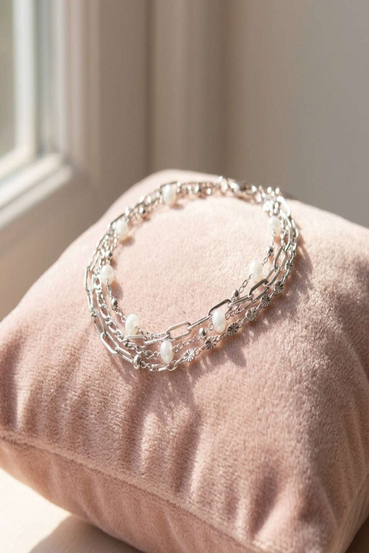 Close-up of a three-layered gold stainless steel bracelet with colored details on a velvet cushion.