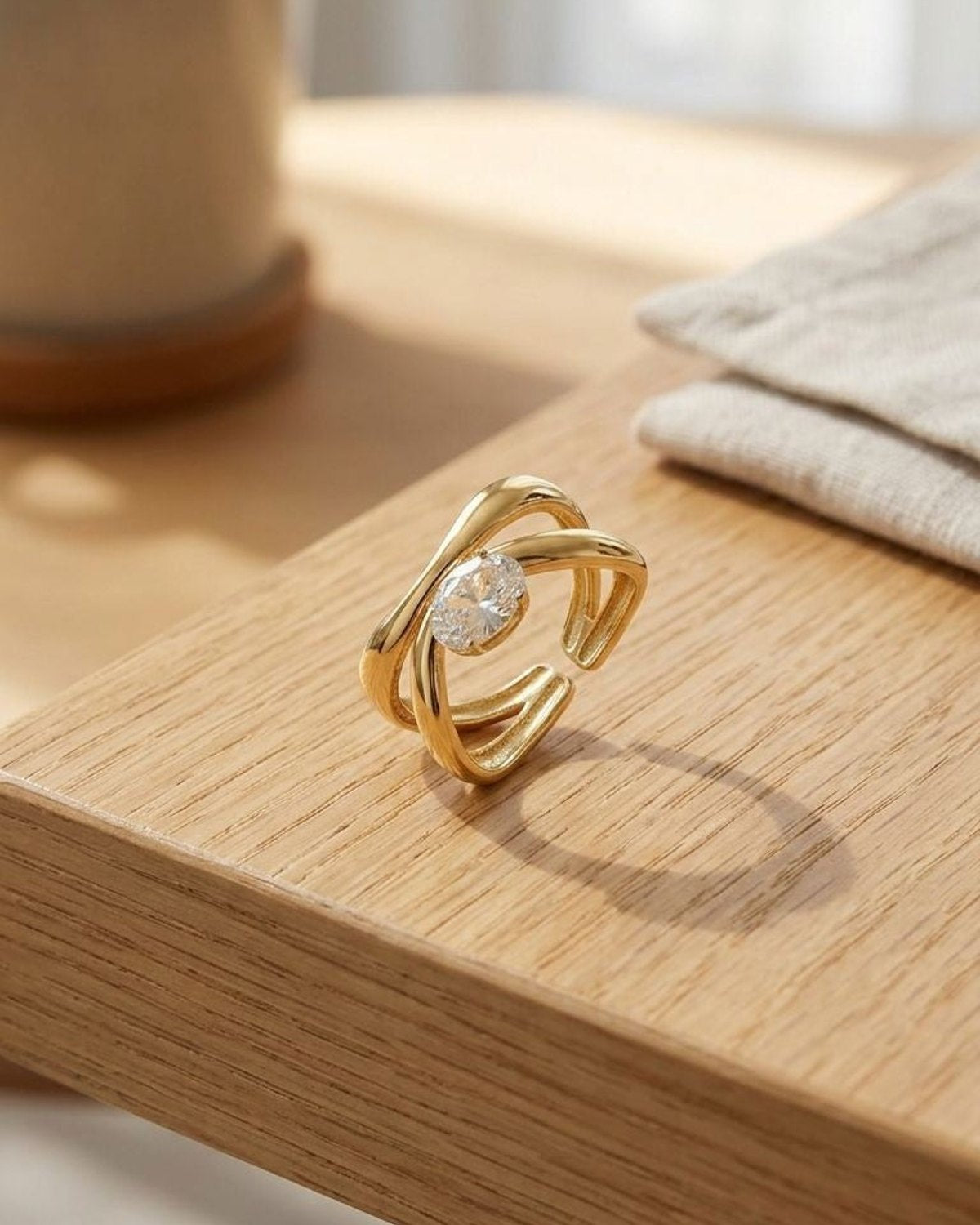 Small Twisted Oval Crystal ring with gold-tone stainless steel and linear detailing, shown on polished surface in natural light.