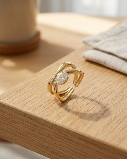 Small Twisted Oval Crystal ring with gold-tone stainless steel and linear detailing, shown on polished surface in natural light.