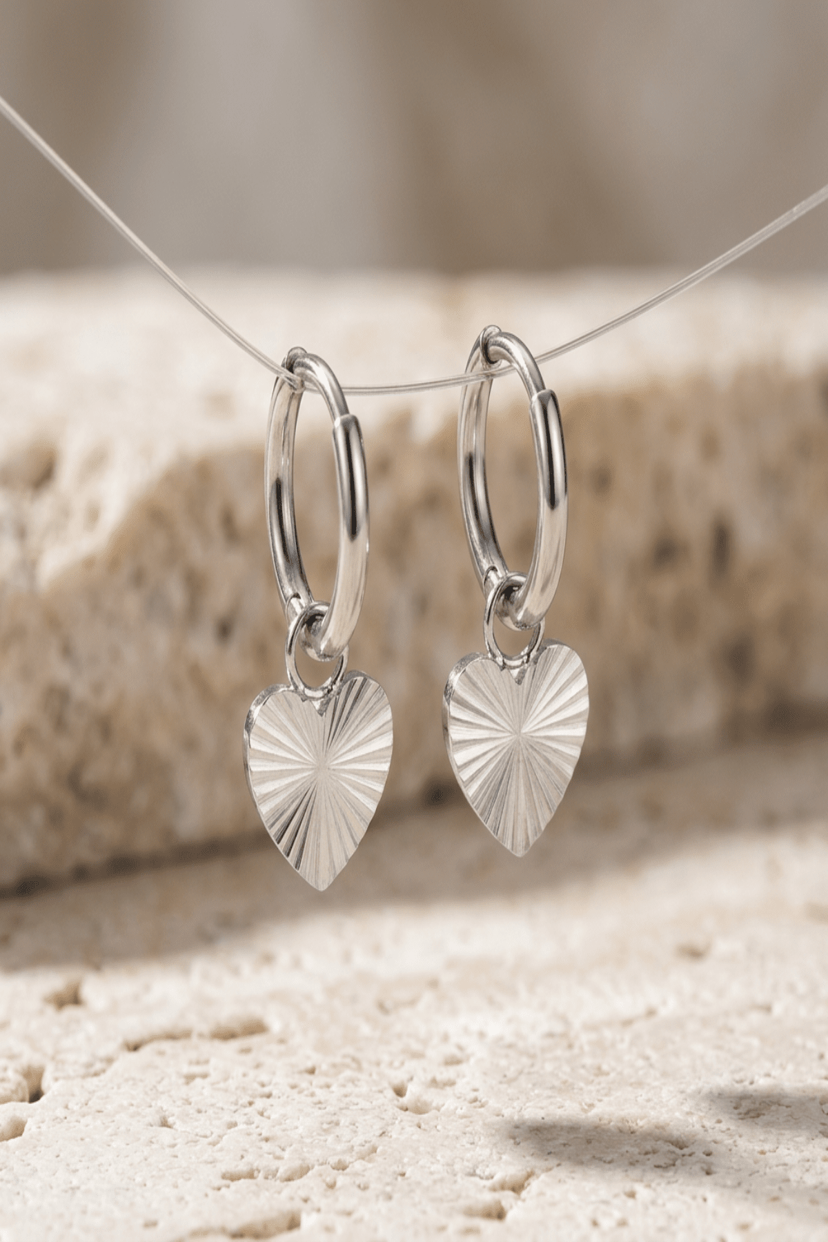 Close-up of radiant heart drop earrings highlighting textured radial pattern and polished stainless steel finish, emphasizing craftsmanship.