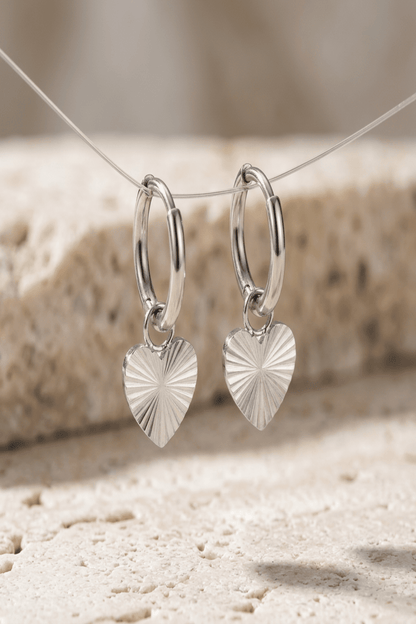 Close-up of radiant heart drop earrings highlighting textured radial pattern and polished stainless steel finish, emphasizing craftsmanship.