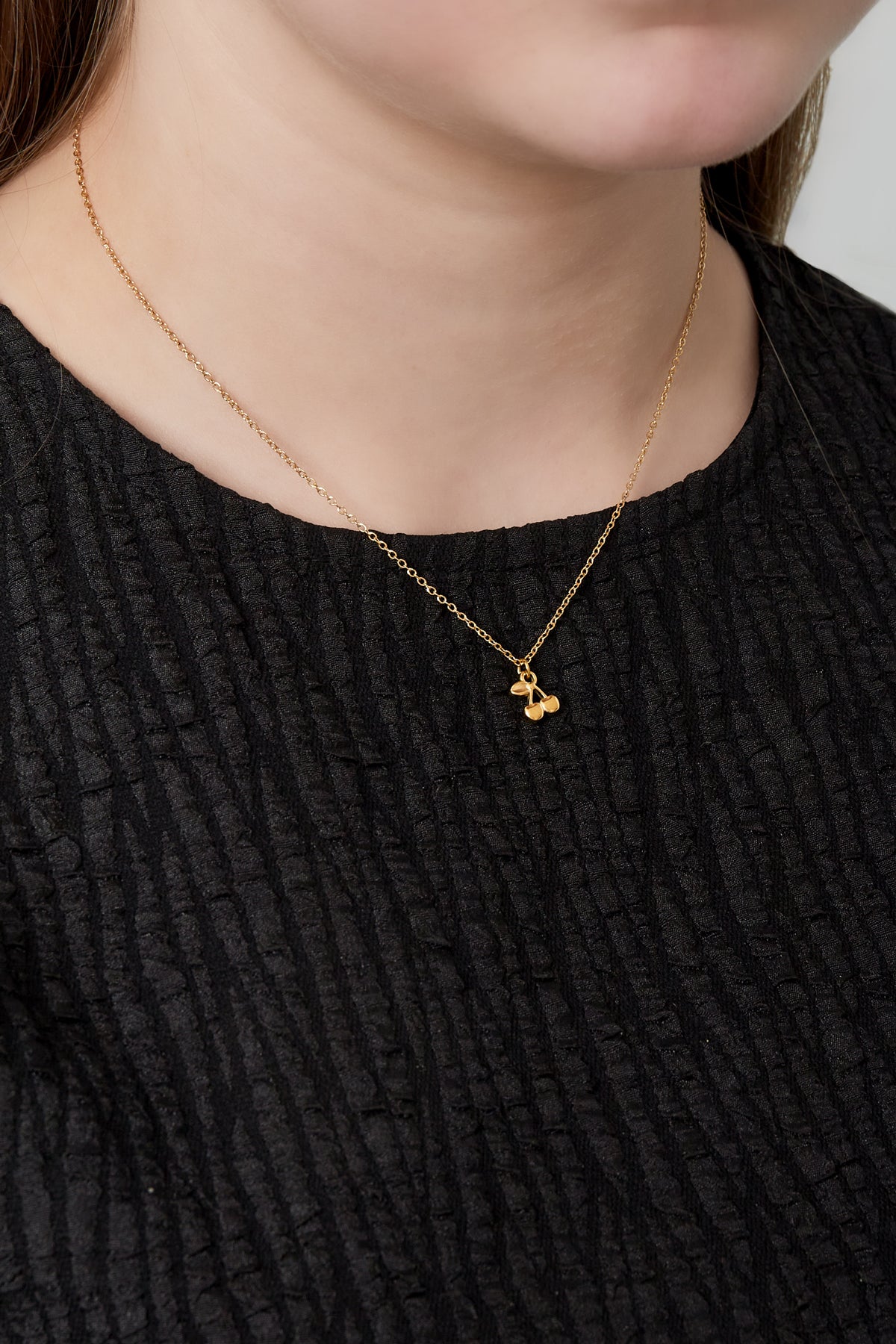 Close-up of a woman wearing the golden cherry pendant necklace with a textured black top