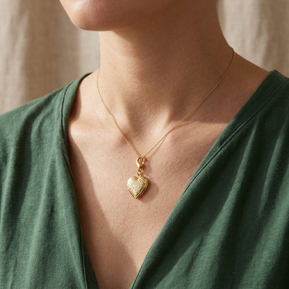 Close-up of a dreamy heart frame charm hanging on a fine chain against a neutral textured fabric, highlighting its stainless steel surface and delicate design.